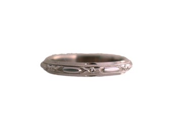 May include: A silver-colored ring with an intricate pattern of repeating shapes and lines. The ring has a slightly rounded profile and a detailed design around the band. The ring is set against a plain white background.