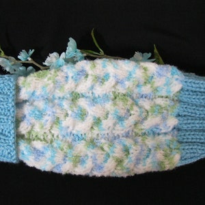 May include: A knitted blue and white cable-knit headband with a light blue ribbed cuff. The center section features a textured pattern with white, blue, and green yarn. The headband is designed to keep the ears warm.