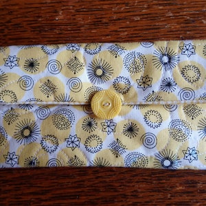 May include: A yellow quilted fabric wallet with a black and white geometric pattern and a yellow button closure.