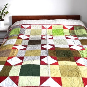 May include: A patchwork quilt featuring a mix of green, red and white squares. The quilt is made from various fabrics and patterns, and is quilted with a simple stitch.
