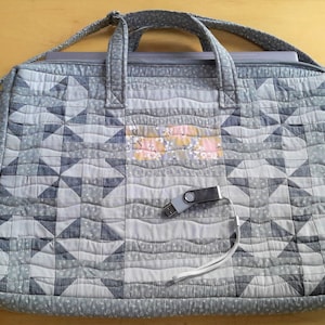 May include: A gray quilted laptop bag with a zipper closure and a small floral fabric pocket on the front. The bag has a long strap and two handles.