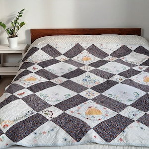 May include: A white and blue quilted bedspread with a diamond pattern and embroidered floral designs. The bedspread is on a wooden bed frame.