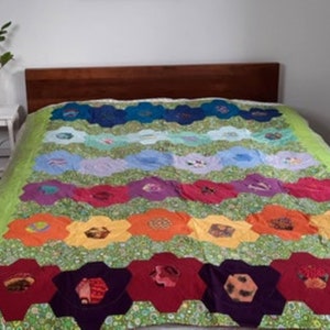 May include: A colorful patchwork quilt with a rainbow pattern. The quilt is made of different fabrics and has a green background. The quilt is on a bed with a wooden headboard.