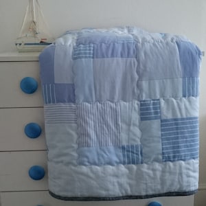 May include: A blue and white patchwork quilt made from repurposed fabric. The quilt is folded and draped over a white dresser with blue knobs.
