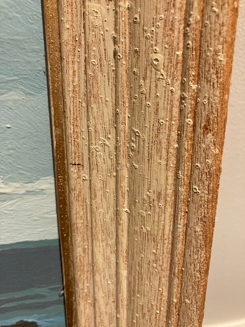 May include: Close-up of a wood frame with a white painted finish and a gold trim. The frame has a distressed look with small holes and imperfections in the paint.