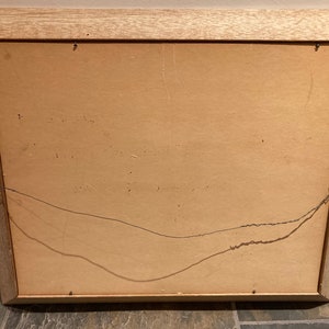 May include: The back of a wooden picture frame with a brown cardboard backing. The frame has a wire hanger attached to the back.