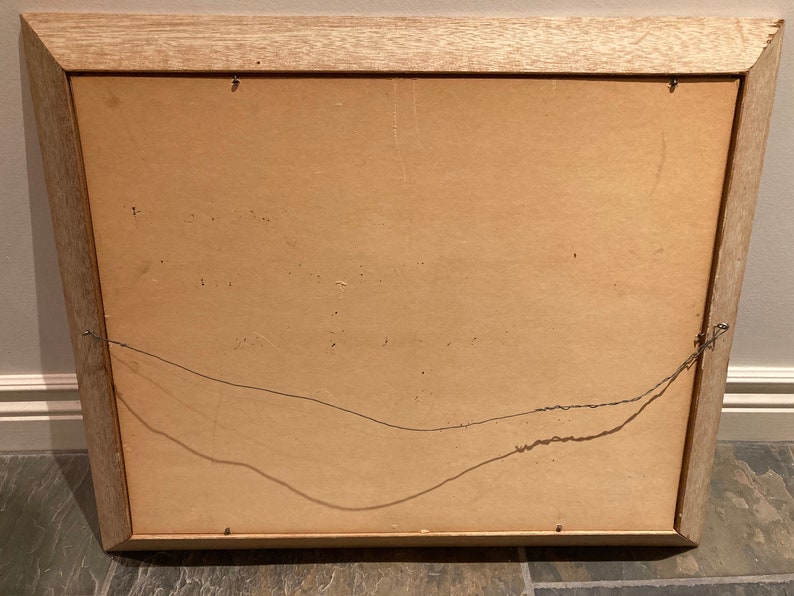 May include: The back of a wooden picture frame with a brown cardboard backing. The frame has a wire hanger attached to the back.