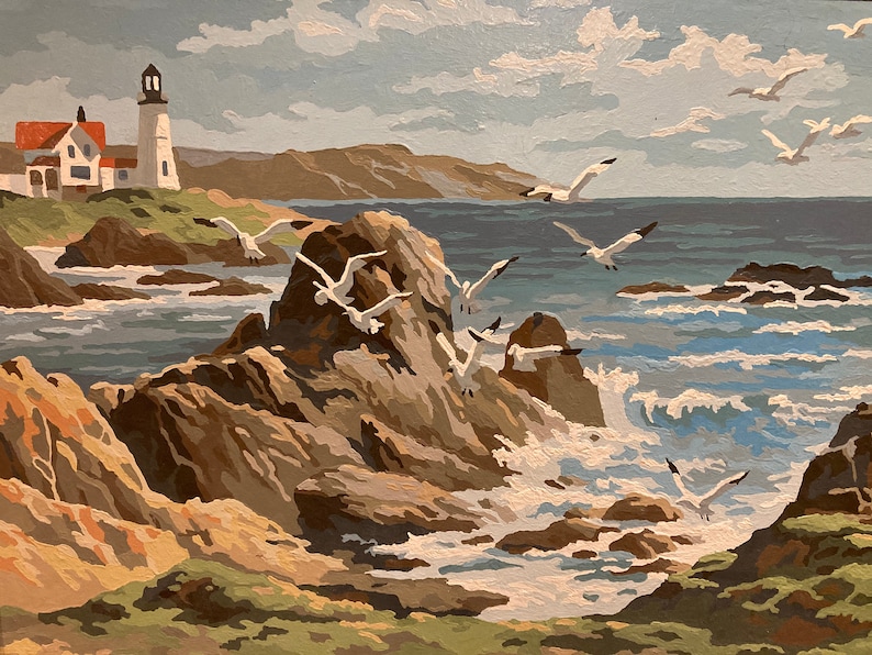 May include: A painting of a white lighthouse on a rocky coastline with seagulls flying overhead. The ocean is a light blue color with white waves crashing against the rocks. The sky is a light blue with white clouds.