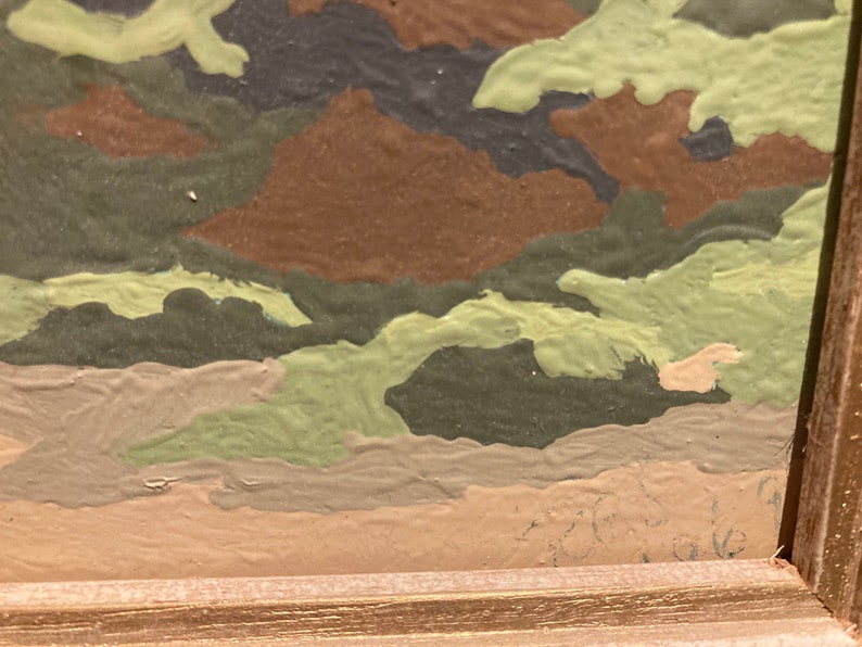 May include: Close-up of a framed painting with a camouflage pattern in shades of green, brown, and beige. The paint is textured and appears to be applied with a brush.