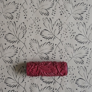 Peut inclure: Un rouleau de peinture rouge avec un motif floral. Le rouleau est sur un fond brun avec un motif floral noir.