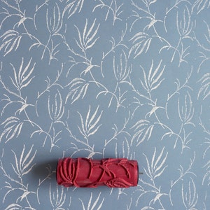 Könnte beinhalten: Eine rote Farbrolle mit einem Blumenmuster. Die Rolle befindet sich auf einem blauen Hintergrund mit einem weißen Blumenmuster.