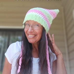 May include: A crochet hat with a pointed top, in light green and pink stripes, with long, pink braided strands. The text "*PATTERN ONLY*" is visible at the top. This is a handmade item.