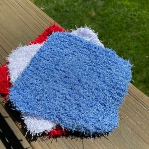 May include: Three crocheted dishcloths in blue, white, and red. The dishcloths are made with a fluffy, textured yarn.