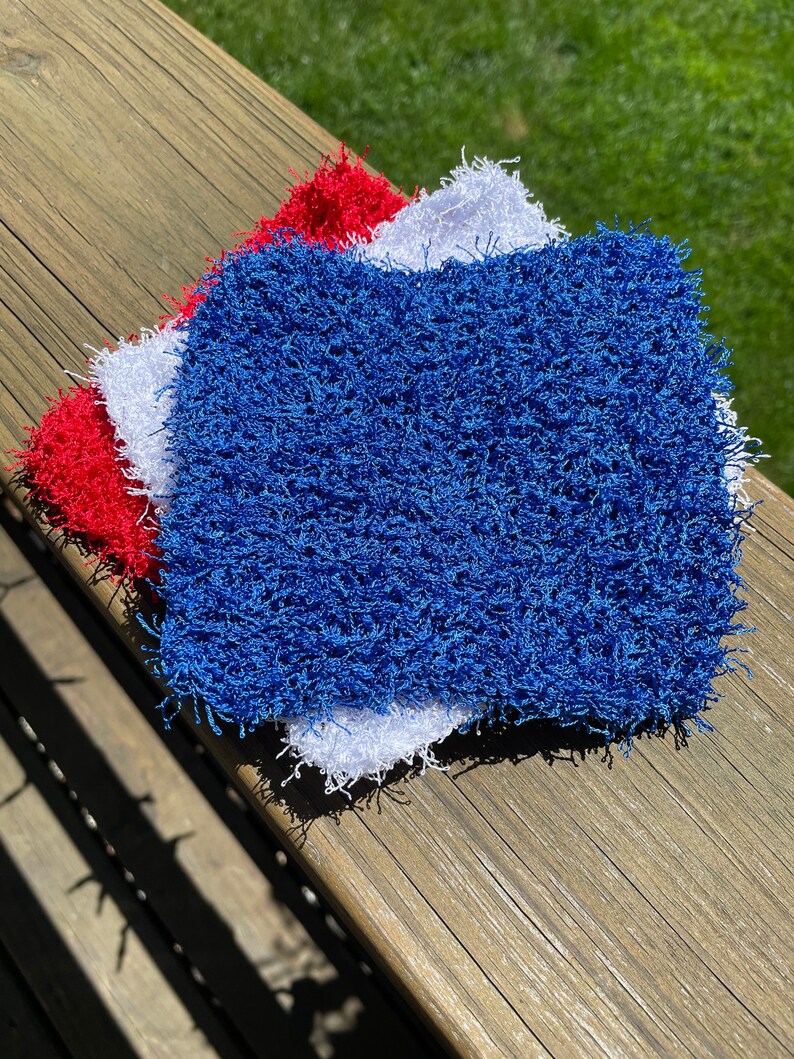 May include: Three crocheted dishcloths in red, white, and blue. The cloths are made of a fluffy, textured yarn.