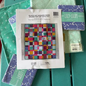 May include: A Block Out Modern Hand Drawn Pop Art Quilt Kit by Krystal Jakelwict. The kit includes fabric squares and a pattern for a 43" x 50" quilt. The quilt design features a colorful patchwork of squares in various colors and patterns. The kit is from Lily-Loom Fabrics.