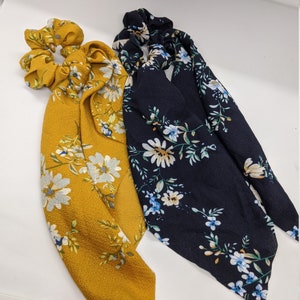 May include: Two hair scrunchies with floral patterns. One is mustard yellow with white flowers and the other is navy blue with white and blue flowers.