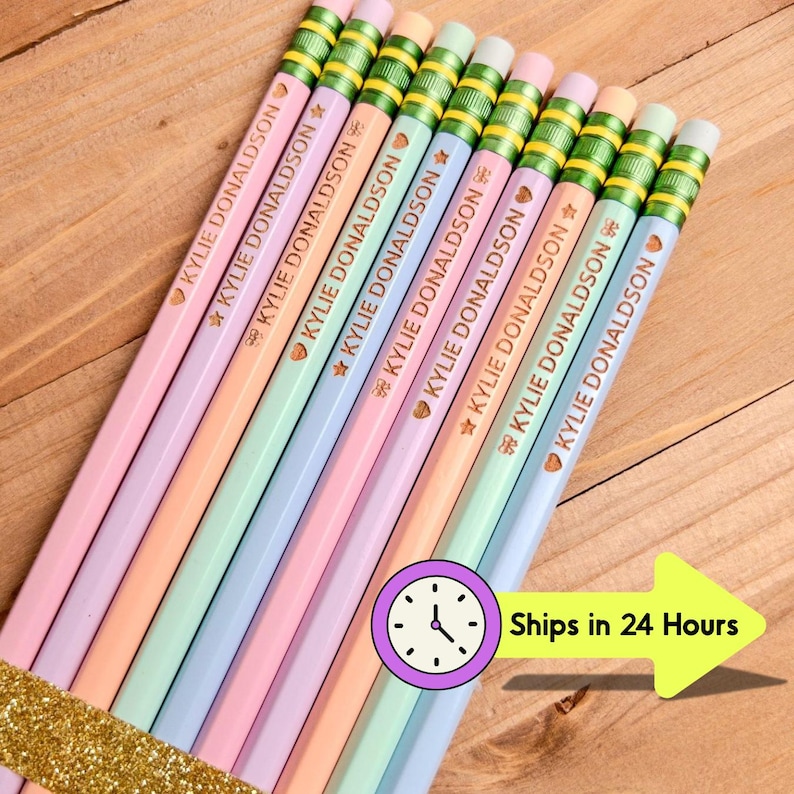 May include: A set of nine pastel-colored pencils arranged in a row, each featuring the name KYLIE DONALDSON printed in gold lettering alongside small heart and star icons. The pencils have green metal ferrules and white erasers at the ends.