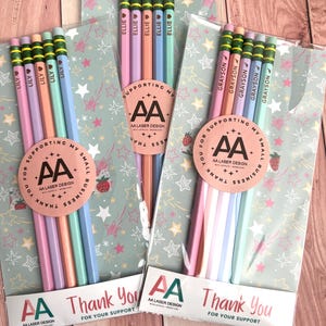 May include: Three sets of five personalized pencils in clear plastic packaging. Each pencil features a green eraser, a gold ferrule, and a name printed in black. The packaging includes a circular sticker with the text AA LASER DESIGN.
