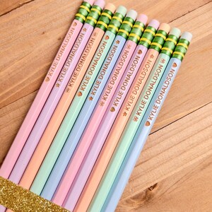 May include: A set of nine pastel-colored pencils arranged in a row, each featuring a metallic green ferrule and a pink eraser. The pencils are imprinted with the name KYLIE DONALDSON in gold lettering, accompanied by a small gold heart icon.