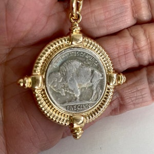 Puede incluir: Un collar de cadena de oro con un colgante que presenta una moneda estadounidense vintage de cinco centavos con un dise&ntilde;o de b&uacute;falo. La moneda est&aacute; rodeada por un marco dorado con un borde texturizado.