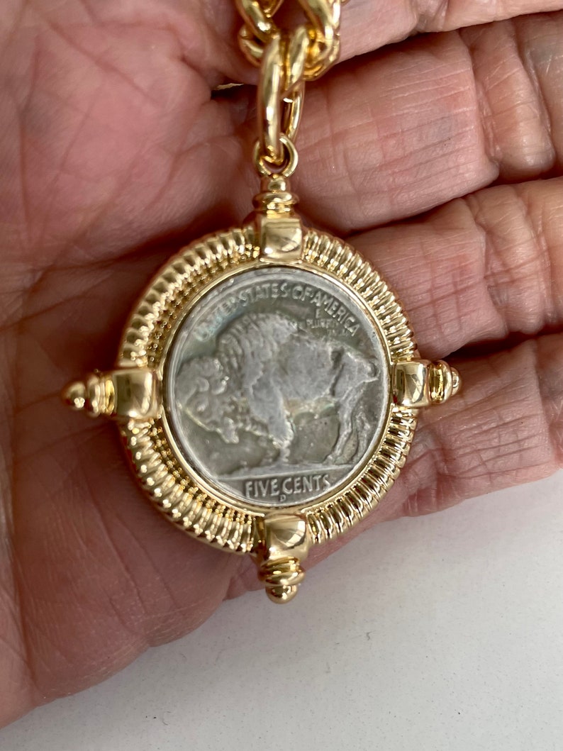 Puede incluir: Un collar de cadena de oro con un colgante que presenta una moneda estadounidense vintage de cinco centavos con un dise&ntilde;o de b&uacute;falo. La moneda est&aacute; rodeada por un marco dorado con un borde texturizado.