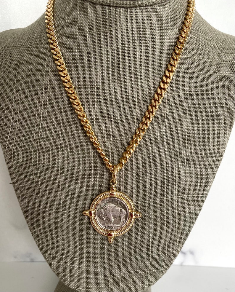 Puede incluir: Un collar de cadena de oro con un colgante que presenta una moneda de n&iacute;quel de b&uacute;falo americano vintage. La moneda est&aacute; rodeada por un marco dorado con cuatro acentos decorativos.