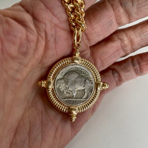 Puede incluir: Un collar de cadena de oro con un colgante que presenta una moneda estadounidense vintage de cinco centavos con un dise&ntilde;o de b&uacute;falo. La moneda est&aacute; rodeada por un marco dorado con acentos decorativos.