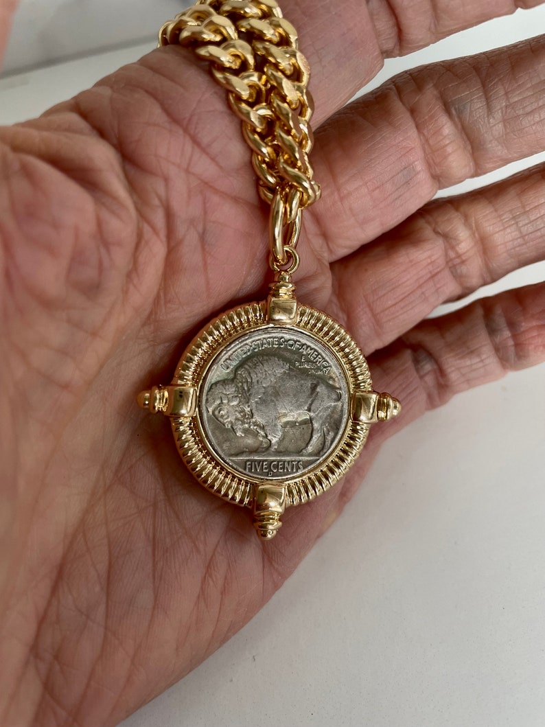 Puede incluir: Un collar de cadena de oro con un colgante que presenta una moneda estadounidense vintage de cinco centavos con un dise&ntilde;o de b&uacute;falo. La moneda est&aacute; rodeada por un marco dorado con acentos decorativos.