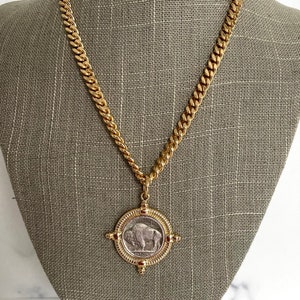 Puede incluir: Un collar de cadena de oro con un colgante que presenta una moneda de n&iacute;quel de b&uacute;falo americano vintage. La moneda est&aacute; rodeada por un marco dorado con cuatro acentos decorativos.