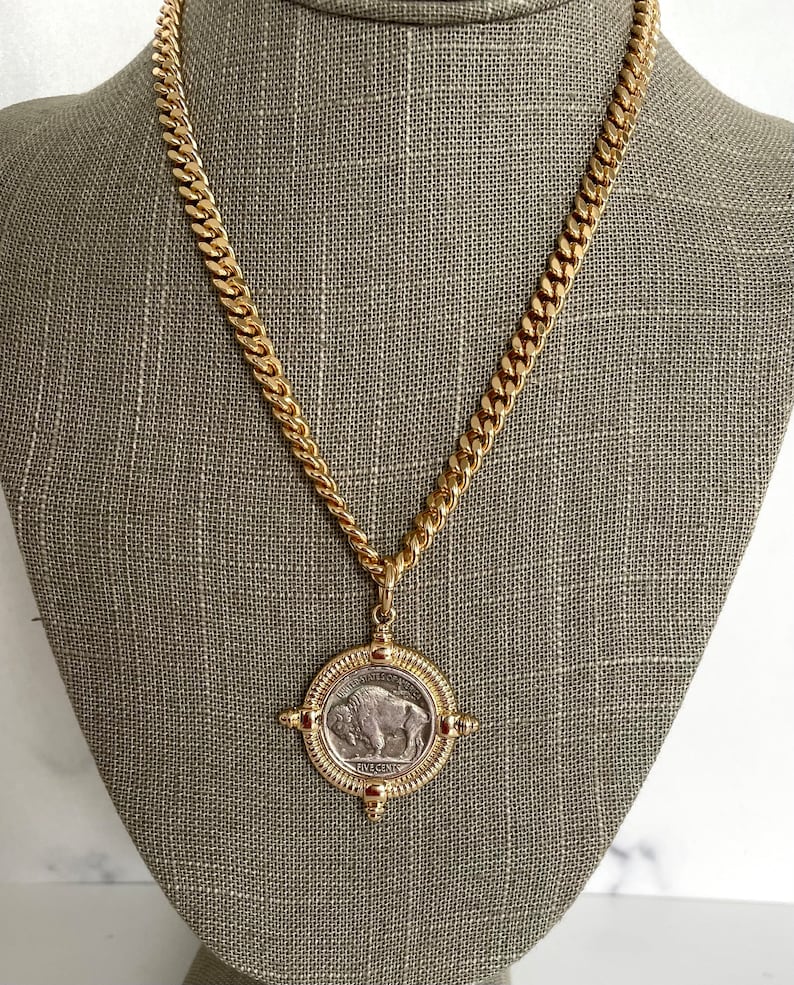 Puede incluir: Un collar de cadena de oro con un colgante que presenta una moneda de n&iacute;quel de b&uacute;falo americano vintage. La moneda est&aacute; rodeada por un marco dorado con cuatro acentos decorativos.