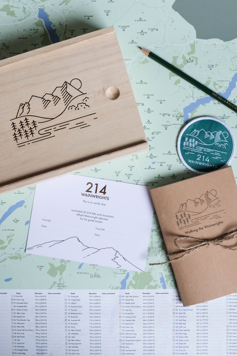 K&ouml;nnte beinhalten: Eine Holzkiste mit einem eingravierten Bergketten-Design auf dem Deckel. Die Kiste enth&auml;lt ein Zertifikat mit dem Text "214 Wainwrights This is to certify that summited all 214 fells and mountains Alfred Wainwright selected for his guide books." Die Kiste enth&auml;lt au&szlig;erdem ein kleines braunes Notizbuch mit dem Text "Walking the Wainwrights" auf dem Umschlag.