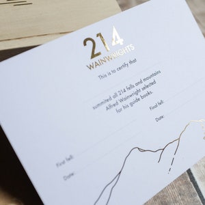 K&ouml;nnte beinhalten: Eine wei&szlig;e Karte mit goldenen Folienbuchstaben, auf der "214 Wainwrights" steht. Die Karte ist ein Zertifikat, das bescheinigt, dass jemand alle 214 Fells und Berge bestiegen hat, die Alfred Wainwright f&uuml;r seine F&uuml;hrer ausgew&auml;hlt hat. Die Karte hat eine Zeile f&uuml;r den letzten Fell und das Datum.