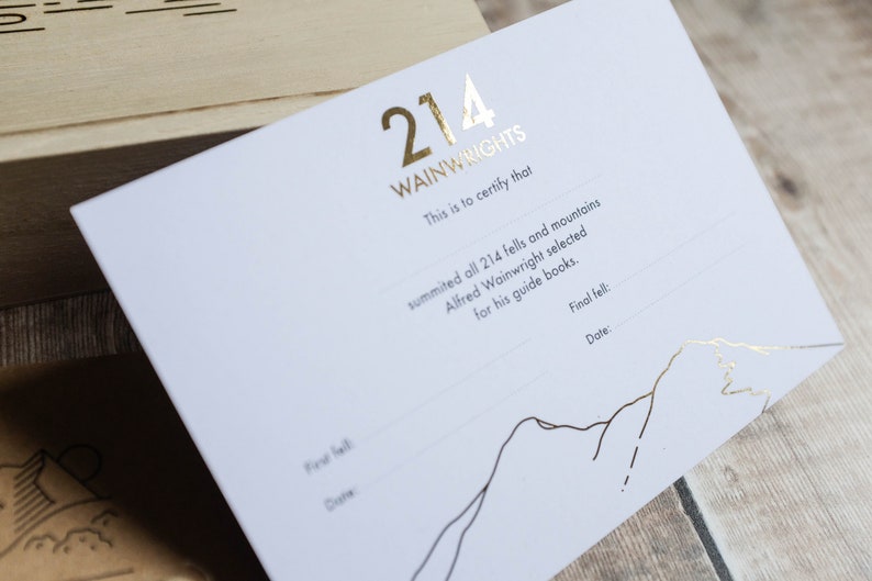 K&ouml;nnte beinhalten: Eine wei&szlig;e Karte mit goldenen Folienbuchstaben, auf der "214 Wainwrights" steht. Die Karte ist ein Zertifikat, das bescheinigt, dass jemand alle 214 Fells und Berge bestiegen hat, die Alfred Wainwright f&uuml;r seine F&uuml;hrer ausgew&auml;hlt hat. Die Karte hat eine Zeile f&uuml;r den letzten Fell und das Datum.