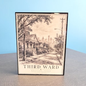 Könnte beinhalten: Eine gerahmte schwarz-weiße Tuschezeichnung einer Straßenszene im Third Ward von Houston, Texas. Das Kunstwerk zeigt Häuser, ein Straßenschild mit der Aufschrift Emancipation Ave und Third Ward sowie eine Skyline. Der Text lautet Third Ward Houston Texas.