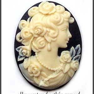 May include: A white cameo featuring a woman with a floral design on a black background. The cameo is oval shaped and has a detailed design.