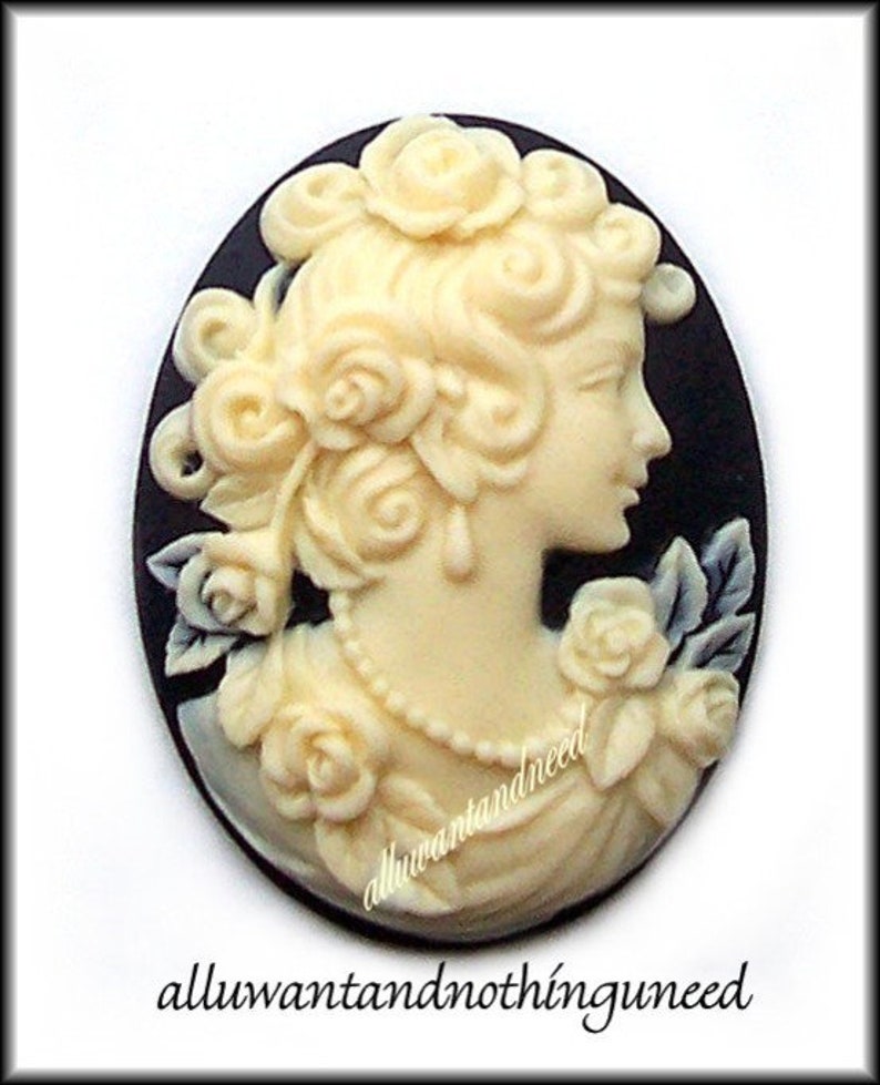 May include: A white cameo featuring a woman with a floral design on a black background. The cameo is oval shaped and has a detailed design.