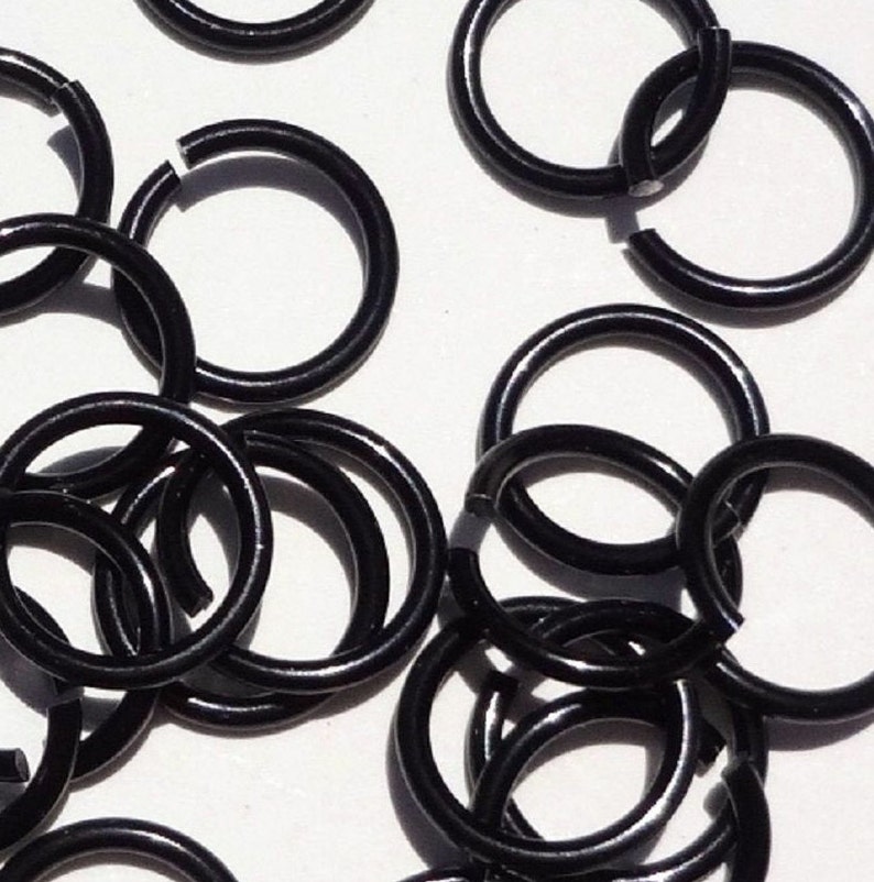 May include: A close-up of a pile of black metal jump rings. The rings are all the same size and are arranged in a random pattern.