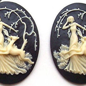 May include: Two black cameo pendants with white raised designs. Each pendant features a woman in a flowing gown with two dogs. The pendants are oval shaped and have a black background.