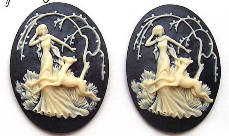 May include: Two black cameo pendants with white raised designs. Each pendant features a woman in a flowing gown with two dogs. The pendants are oval shaped and have a black background.