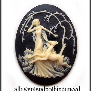 May include: A black cameo with a white raised design of a woman in a flowing dress with a deer beside her. The cameo is set against a black background with a white tree branch design.