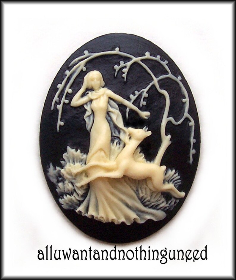 May include: A black cameo with a white raised design of a woman in a flowing dress with a deer beside her. The cameo is set against a black background with a white tree branch design.