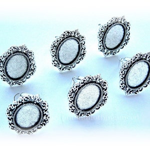May include: Six silver oval-shaped rings with ornate filigree designs and a white glitter center.