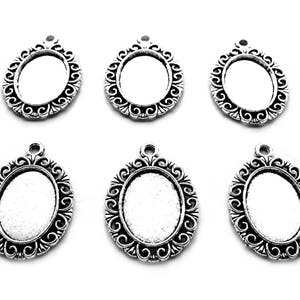 May include: Six silver oval-shaped pendant trays with ornate filigree designs. The trays are designed to hold a small cameo or other decorative item.