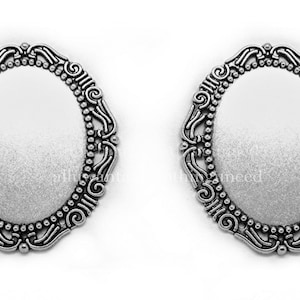 May include: Two silver oval-shaped metal frames with ornate designs. The frames are blank and ready to be used for crafting projects.
