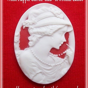 May include: White cameo featuring a flapper girl wearing a hat and a pearl necklace. The cameo is 40 x 30 mm and is set on a red background.