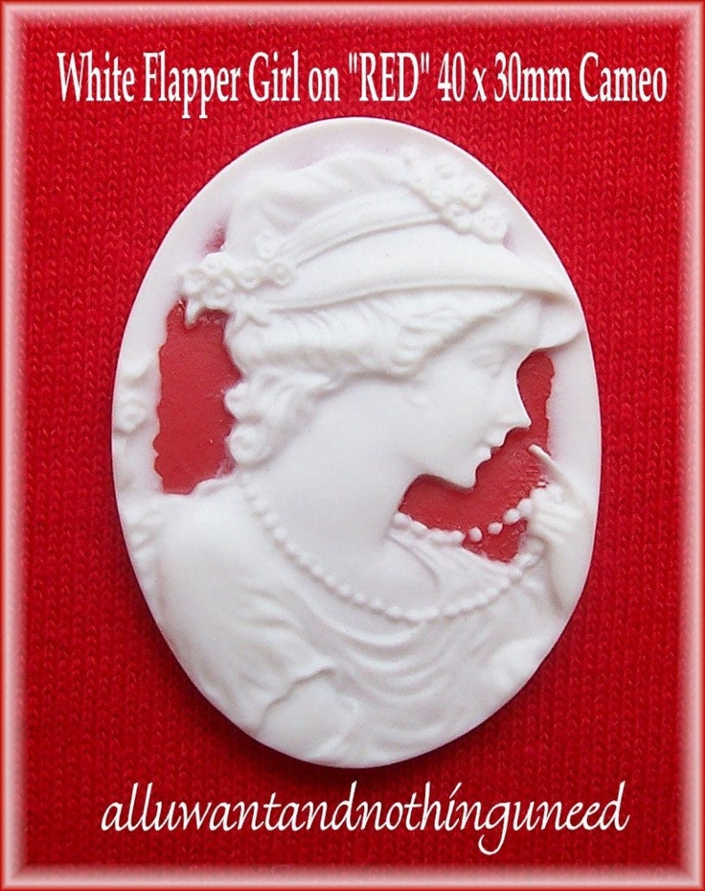 May include: White cameo featuring a flapper girl wearing a hat and a pearl necklace. The cameo is 40 x 30 mm and is set on a red background.