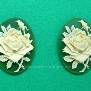 May include: A pair of white cameo earrings with a green background. Each earring features a detailed carving of a white rose with leaves.