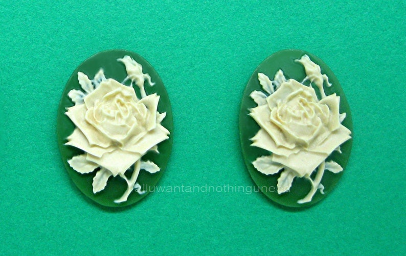 May include: A pair of white cameo earrings with a green background. Each earring features a detailed carving of a white rose with leaves.