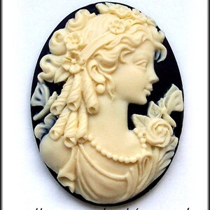 May include: A white cameo featuring a woman's profile with a floral design. The cameo is set in a black oval background.