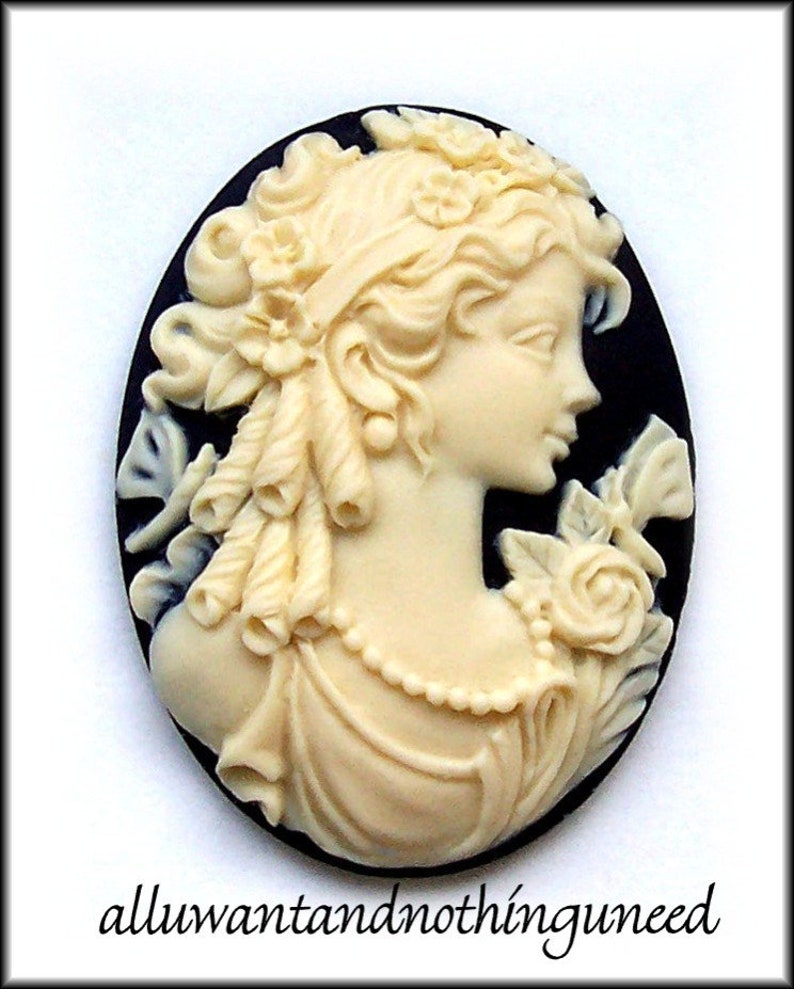 May include: A white cameo featuring a woman's profile with a floral design. The cameo is set in a black oval background.